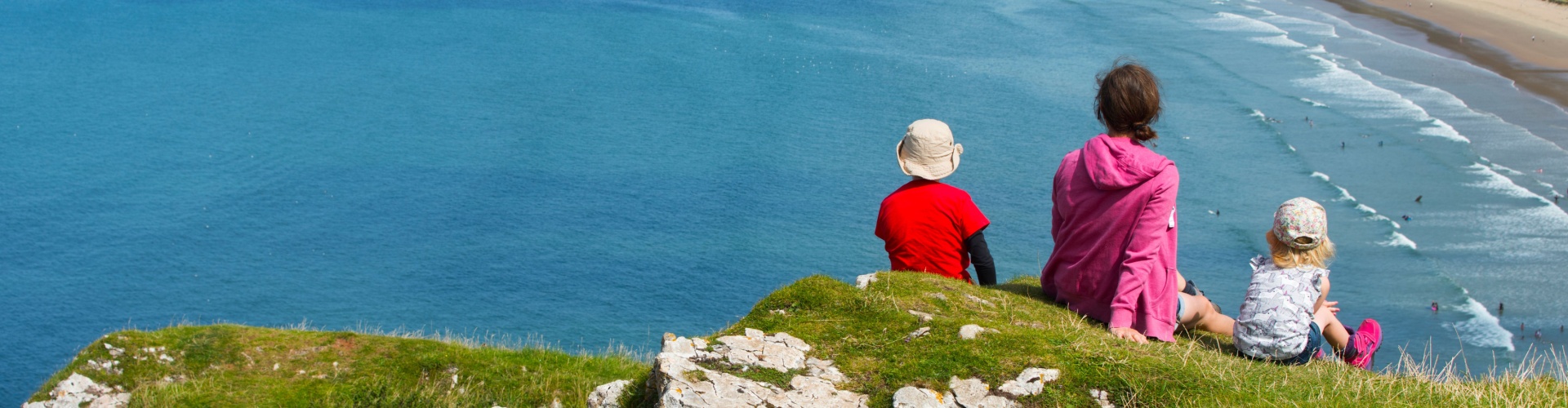 A family sitting on a clifftop overlooking a beach.