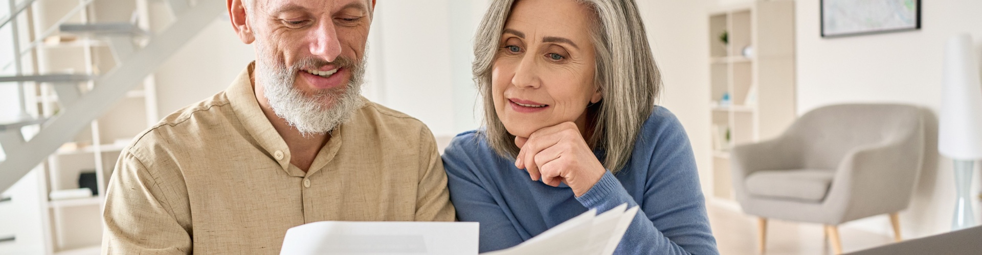 A senior couple sit at a laptop comparing multiple documents