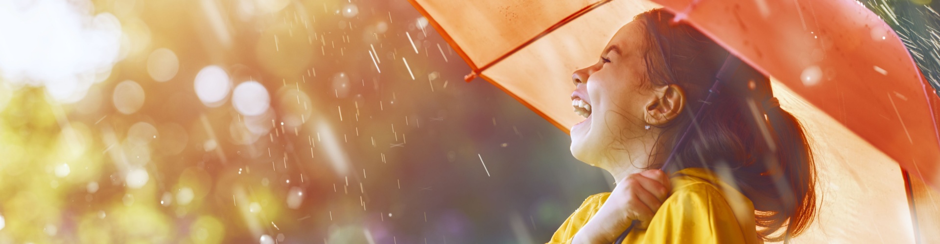 A girl laughing in the rain under an umbrella.
