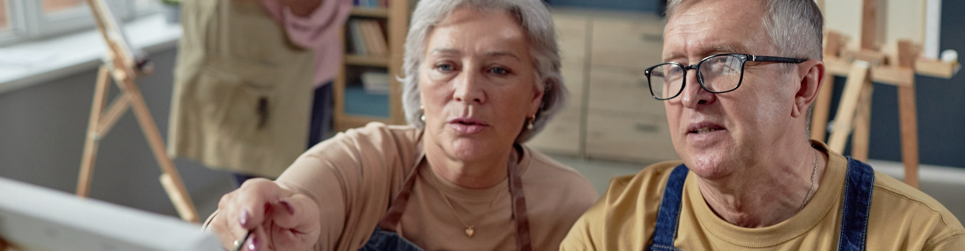 An older couple painting at an easel together.