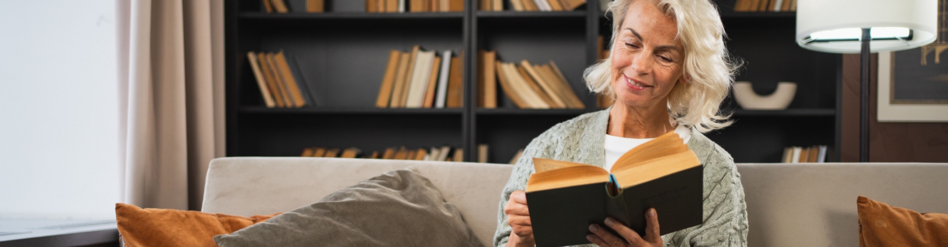 Smiling lady sitting on a sofa reading a book