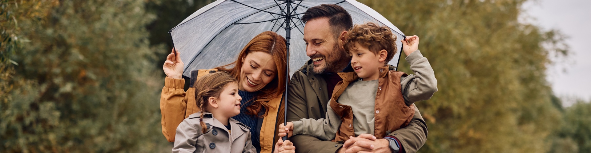 A young family sheltering under an umbrella and smiling