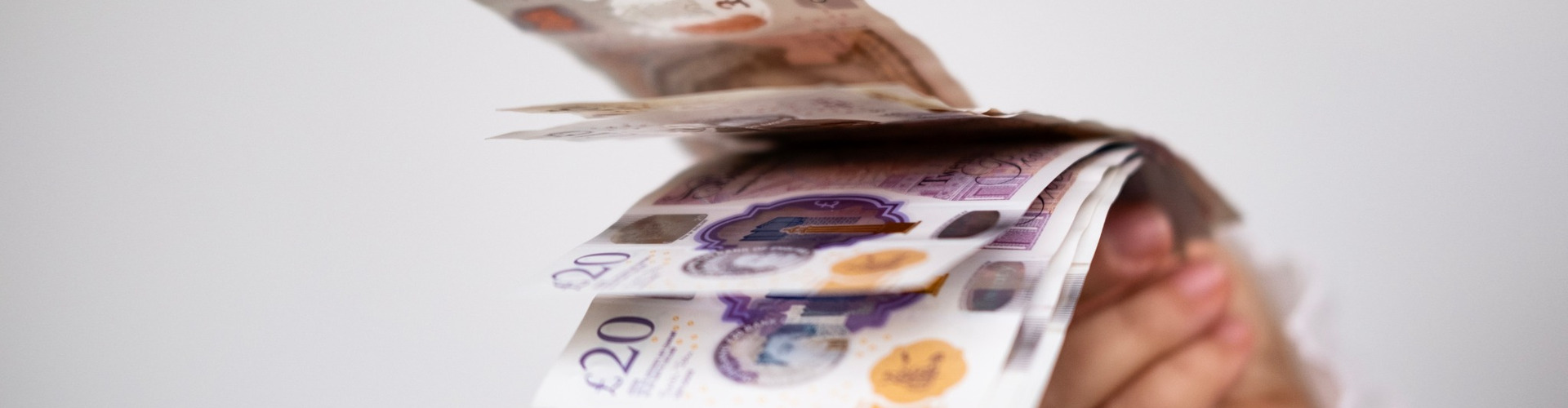 A hand holding UK bank notes.
